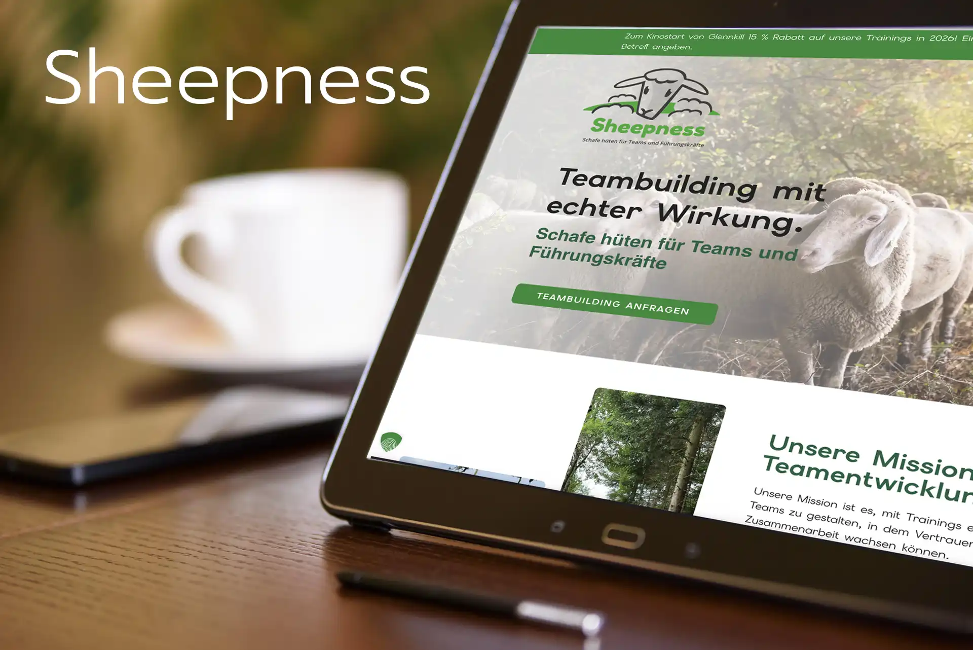Tablet im Querformat auf einem Holztisch, auf dem die Webseite von Sheepness zu sehen ist, im Hintergrund unscharf eine weiße tasse